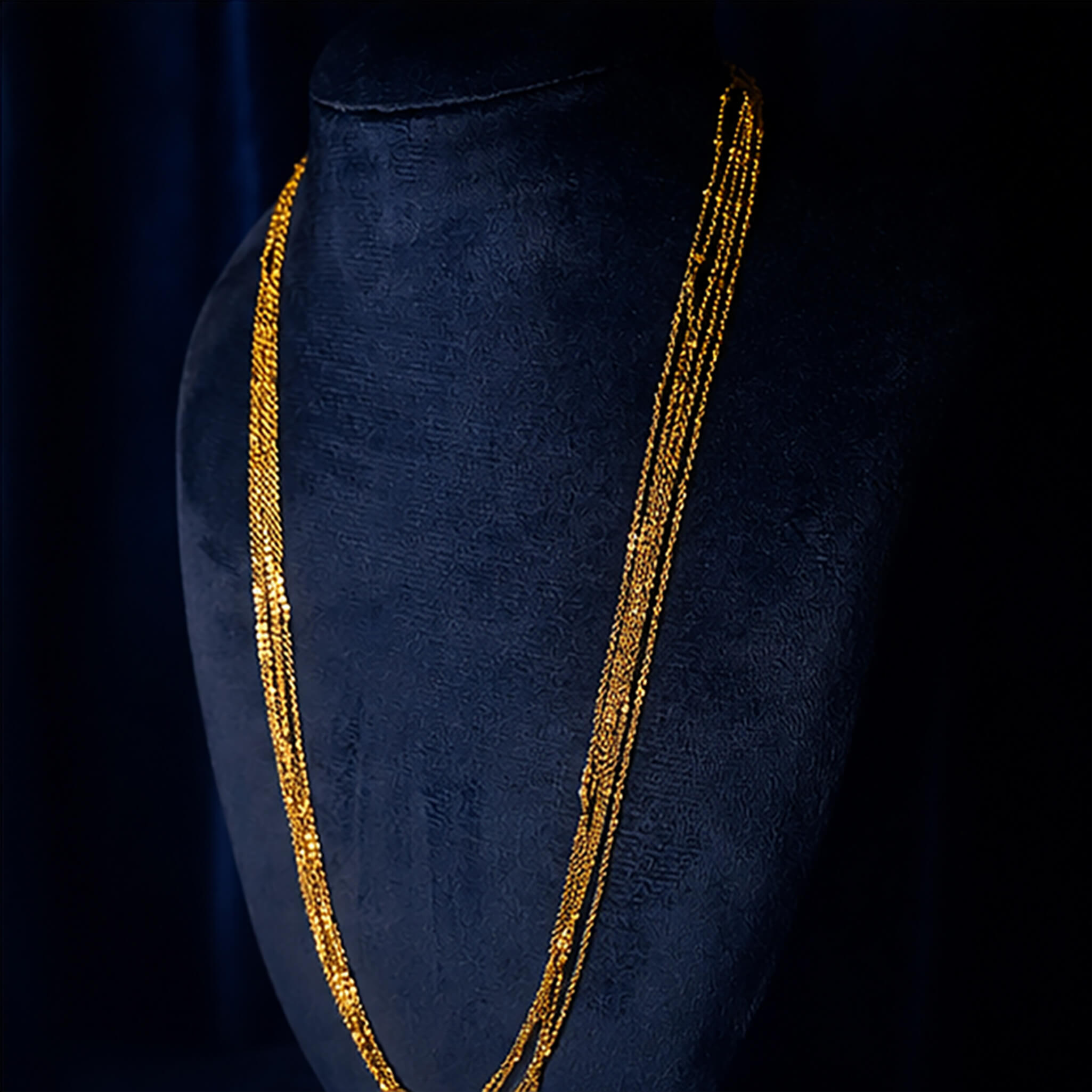 Elegant gold-tone multi-strand long chain displayed on a black jewelry bust against a royal blue velvet background.