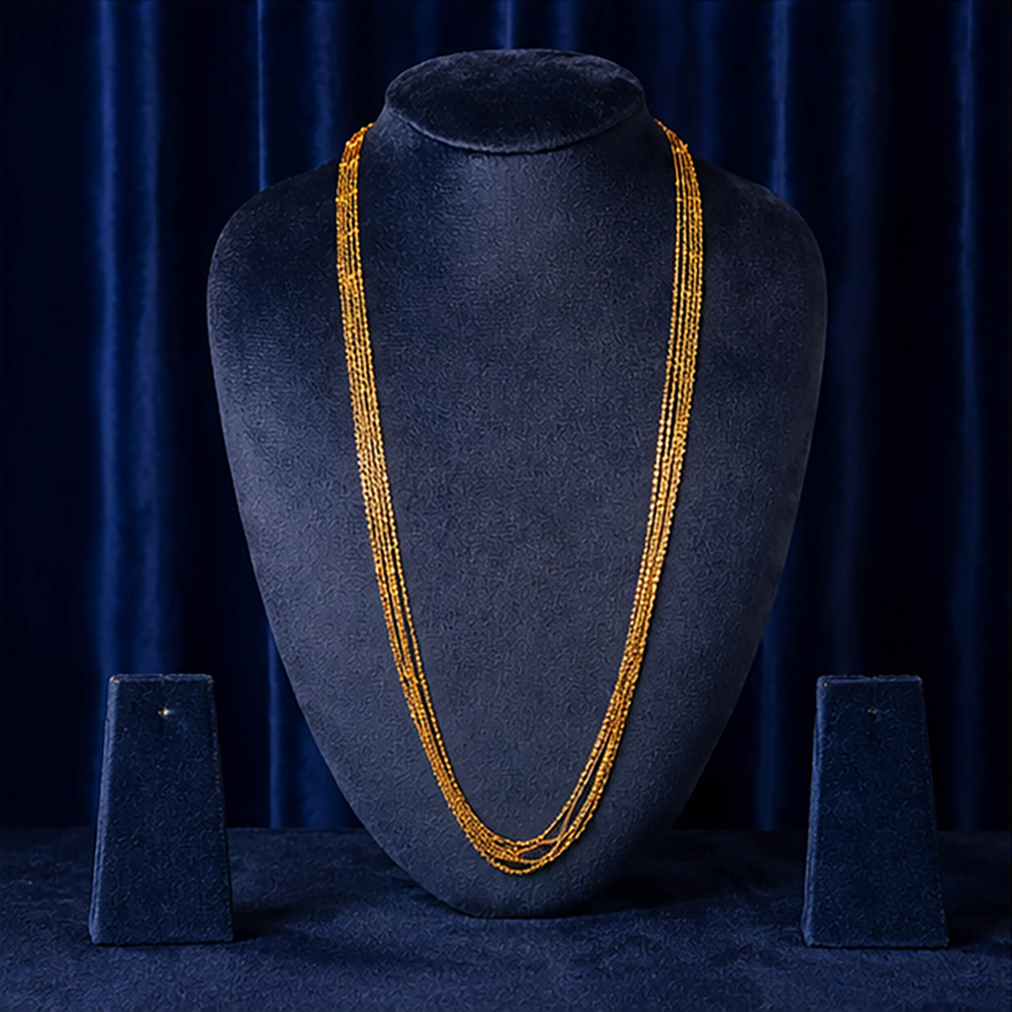 Elegant gold-tone multi-strand long chain displayed on a black jewelry bust against a royal blue velvet background.