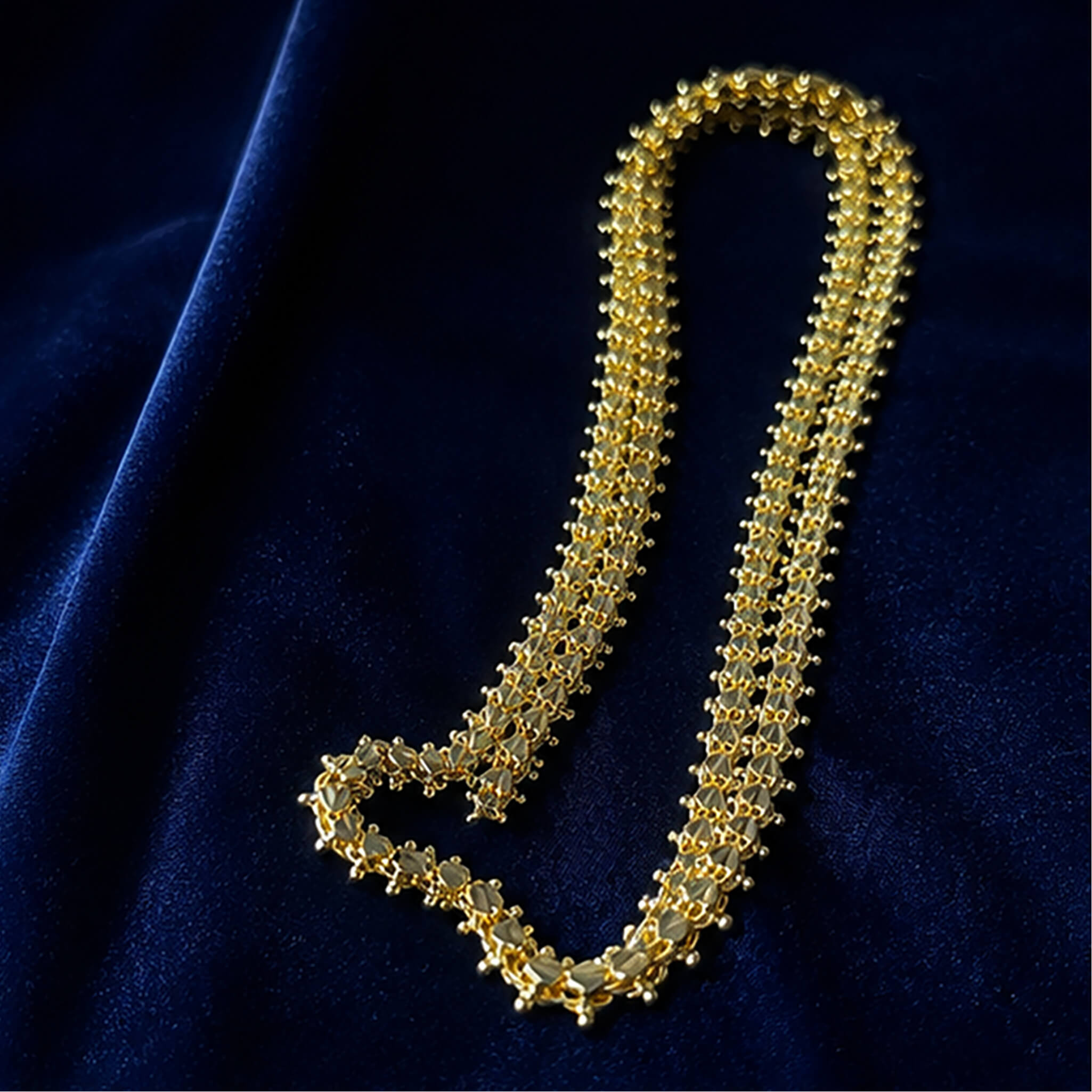 Elegant gold-tone heritage long chain with intricate bead detailing displayed on a luxurious navy blue fabric background.