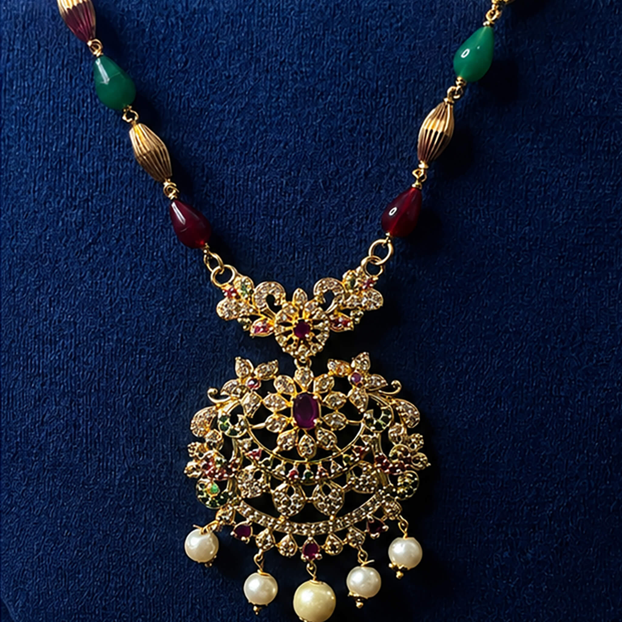 Gold-tone multicolor beaded necklace with an ornate filigree pendant and pearl drops displayed on a luxury blue jewelry bust.