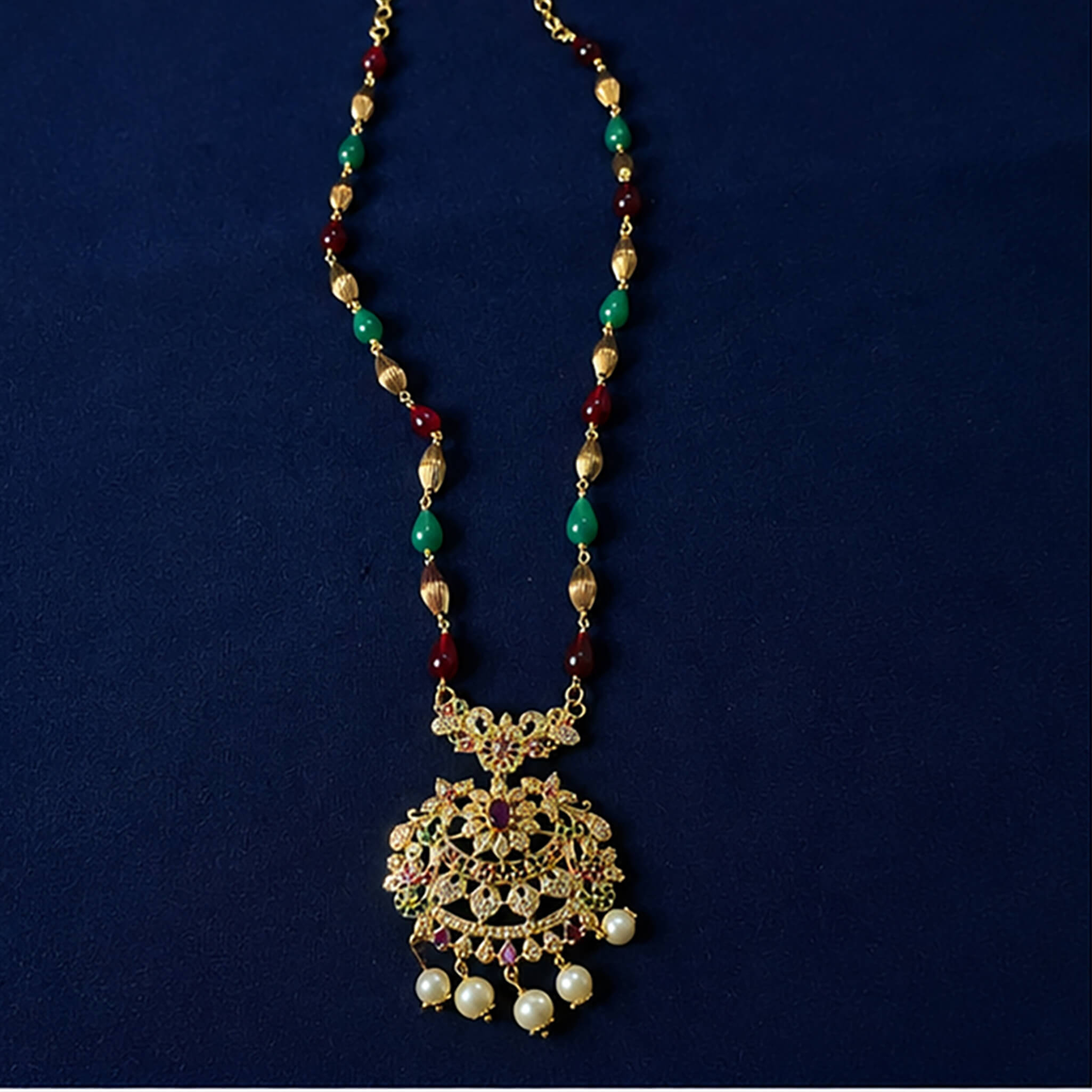 Gold-tone multicolor beaded necklace with an ornate filigree pendant and pearl drops displayed on a luxury blue jewelry bust.