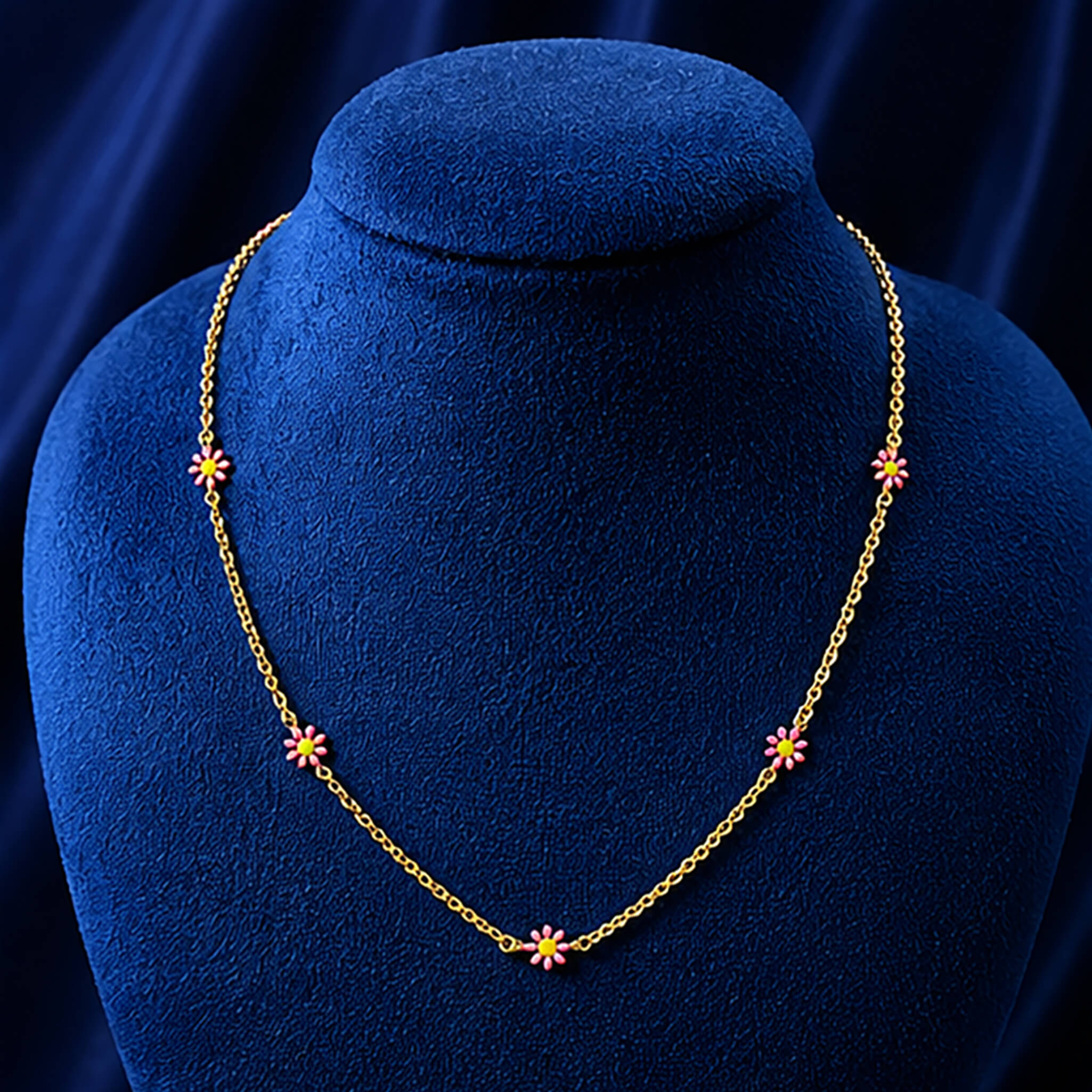 Gold-tone floral necklace with pink flower charms displayed on a royal blue velvet jewelry bust.