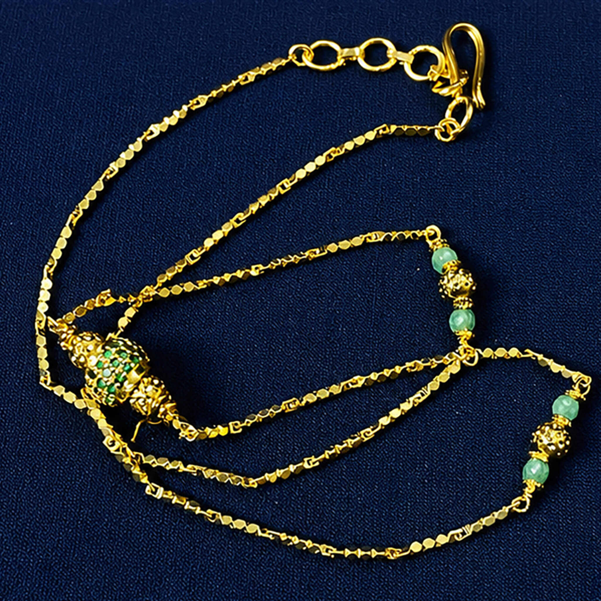 Gold-tone necklace with green beads and decorative centerpiece displayed on a royal blue velvet jewelry bust.