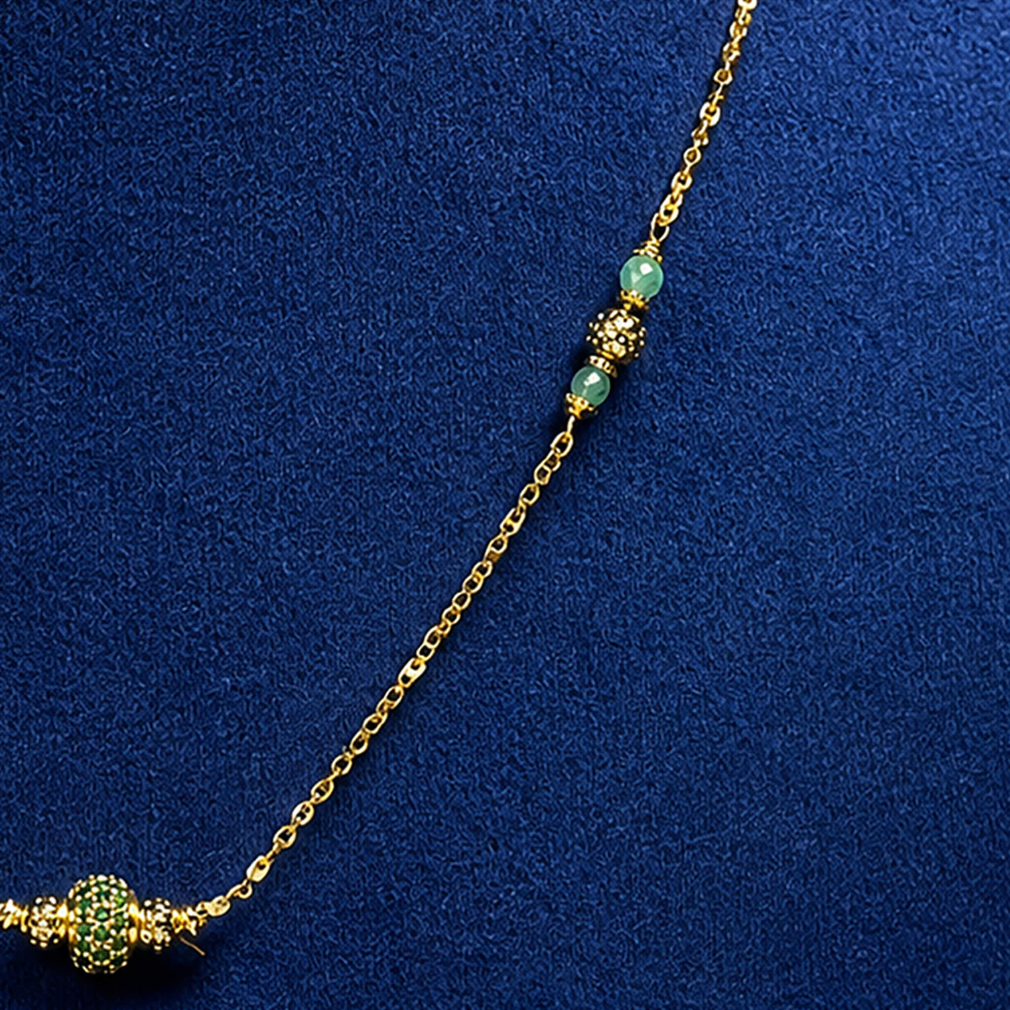 Gold-tone necklace with green beads and decorative centerpiece displayed on a royal blue velvet jewelry bust.
