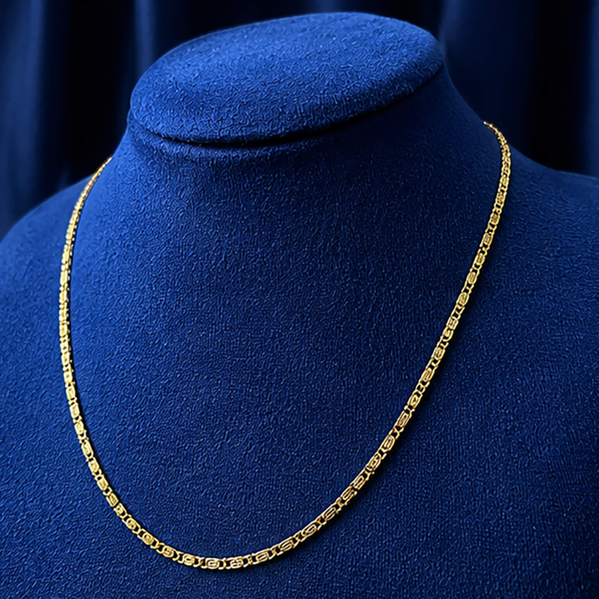 Elegant gold-tone patterned link chain displayed on a royal blue velvet jewelry bust.
