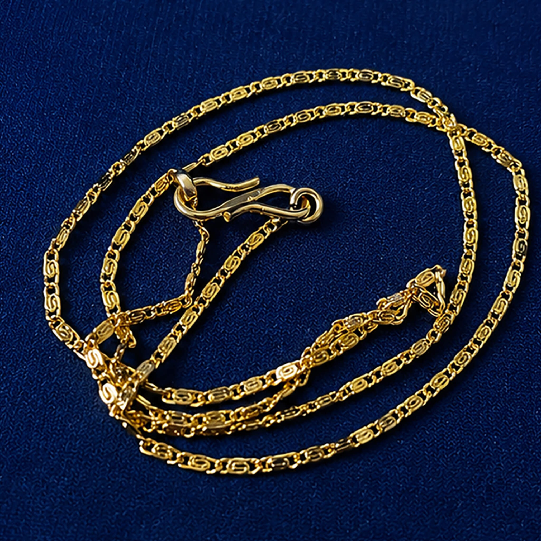 Elegant gold-tone patterned link chain displayed on a royal blue velvet jewelry bust.