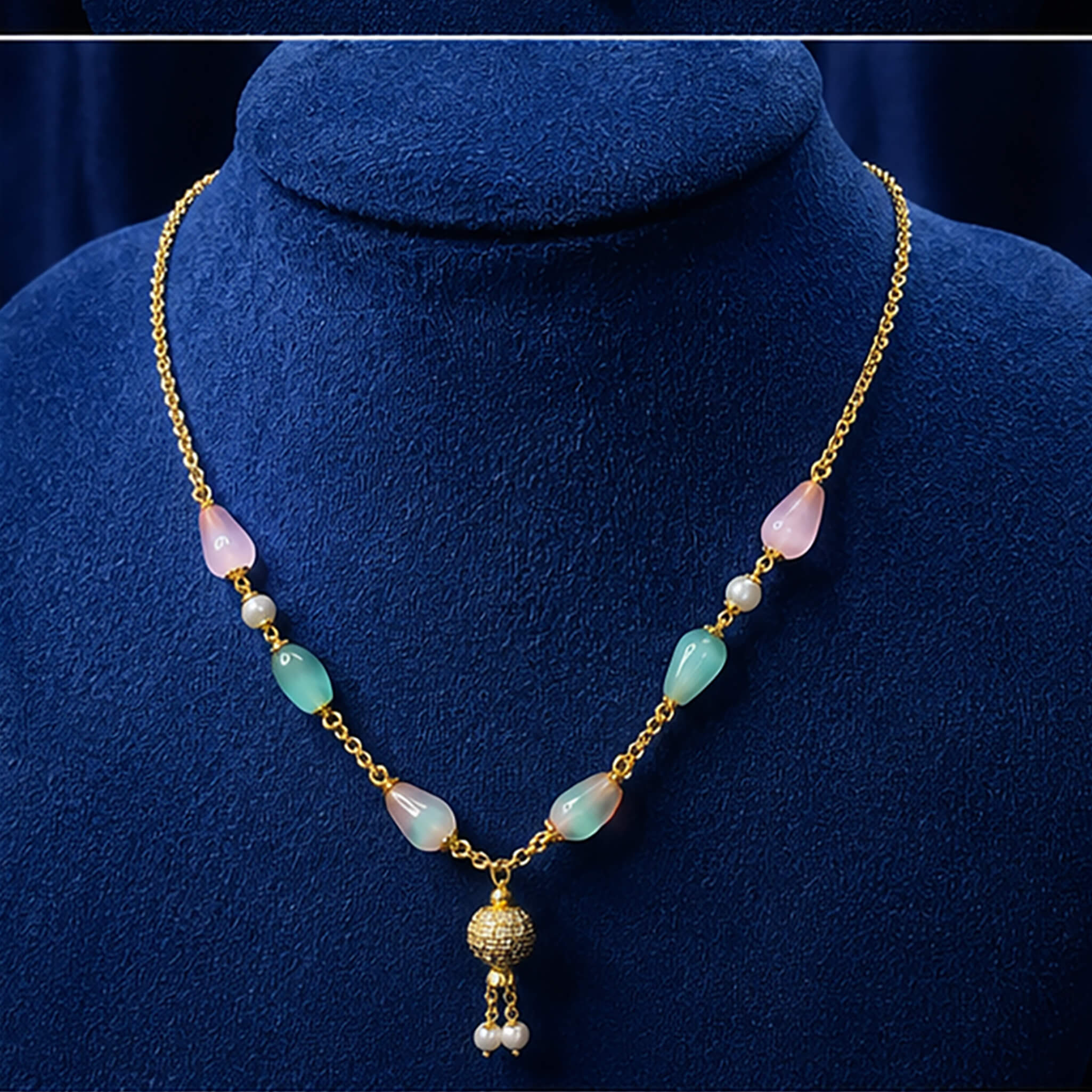 Gold-tone necklace with pastel pink and mint-green beads, pearl accents, and decorative pendant displayed on a royal blue velvet jewelry bust.