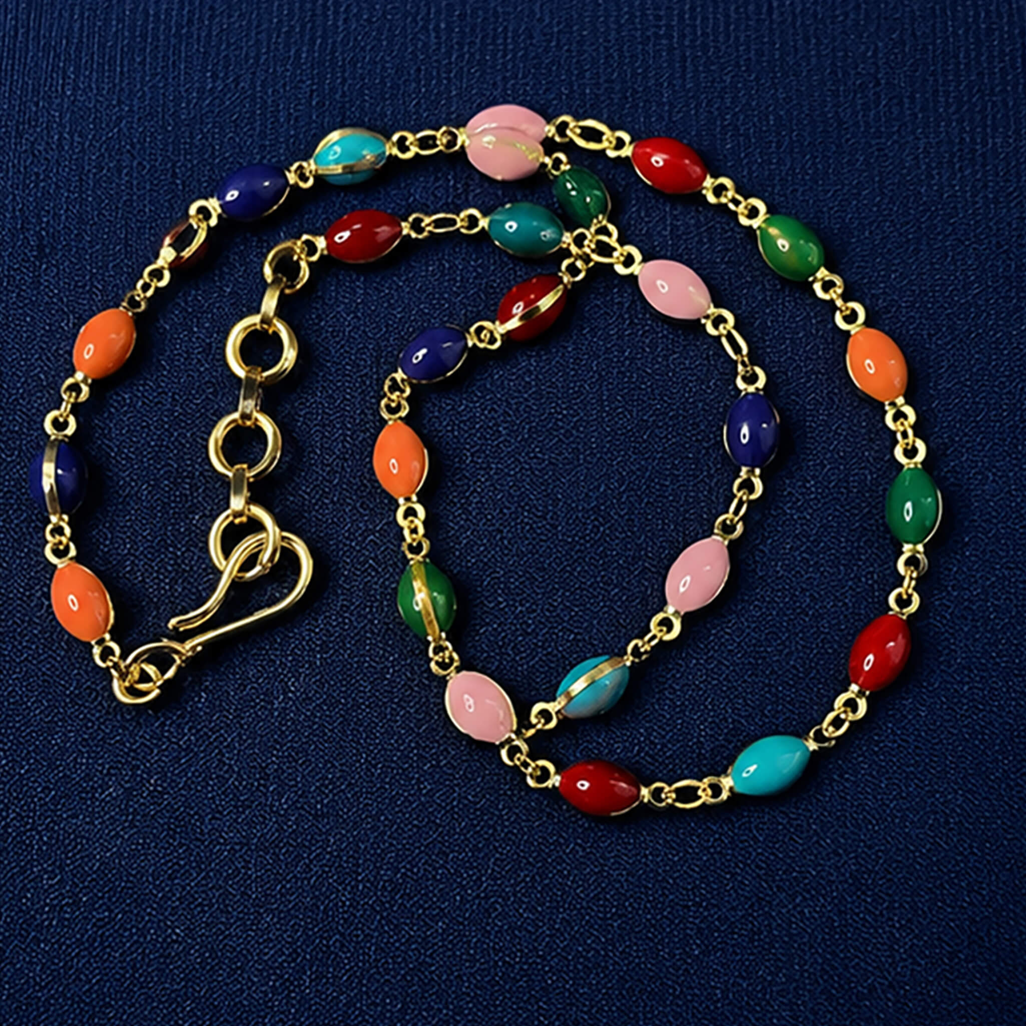 Gold-tone necklace featuring vibrant multicolored beads displayed on a royal blue velvet jewelry bust.