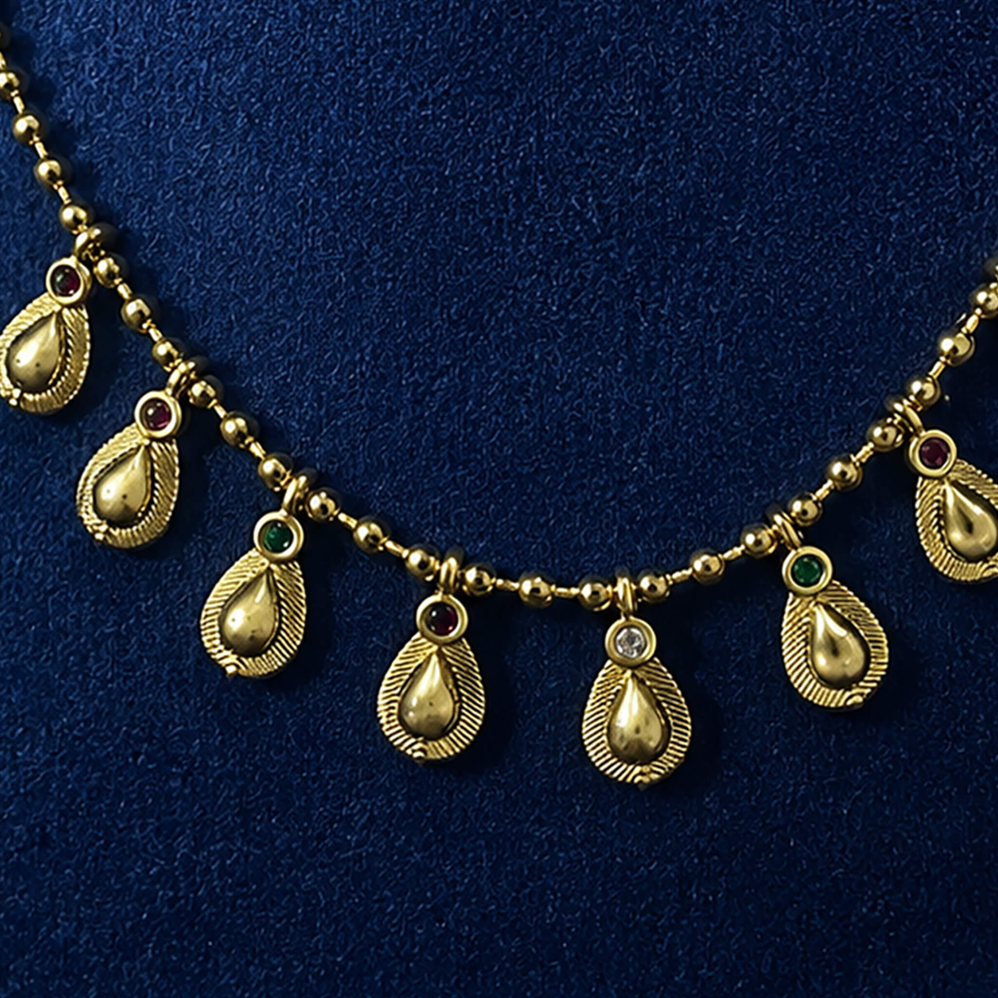 Gold-tone necklace with dangling teardrop charms displayed on a royal blue velvet jewelry bust.