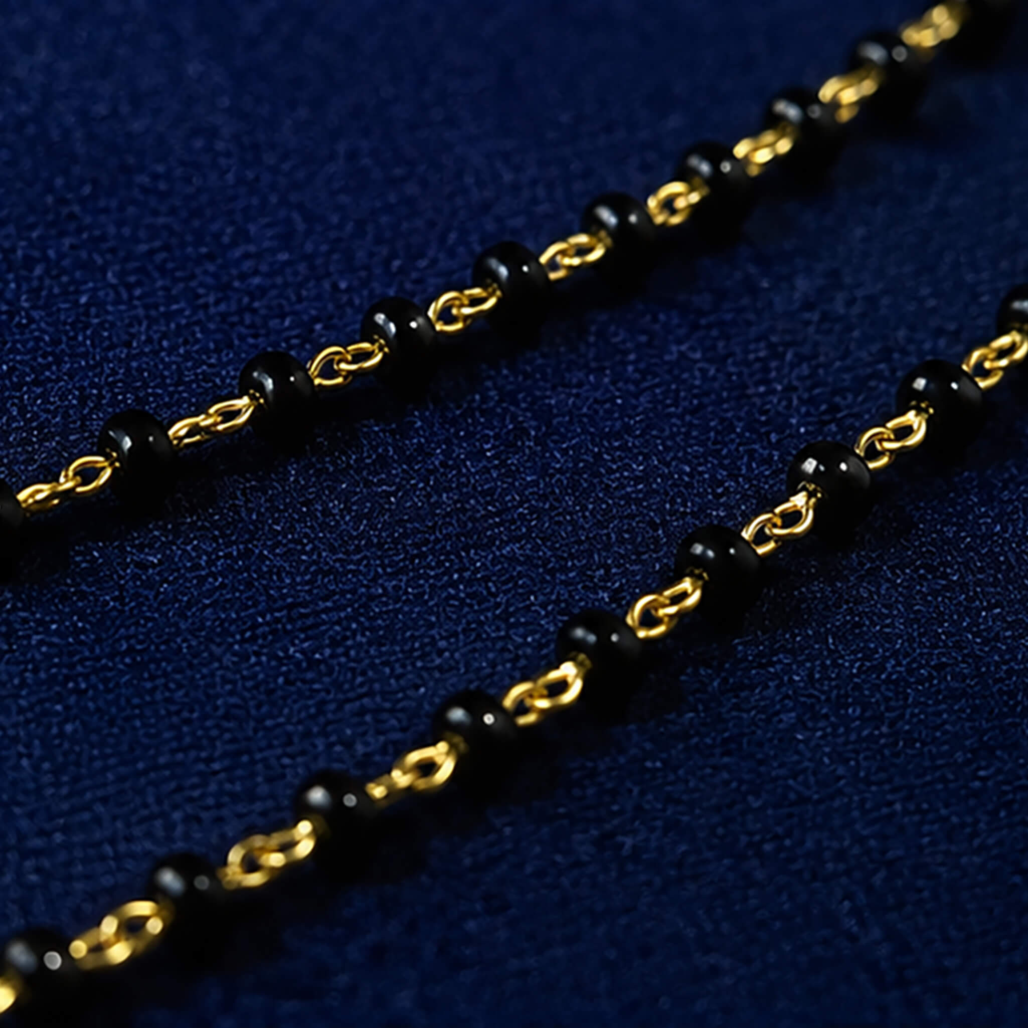 Black-bead mangalsutra necklace with ruby-red stone pendant and dangling charms displayed on a royal blue velvet jewelry bust.