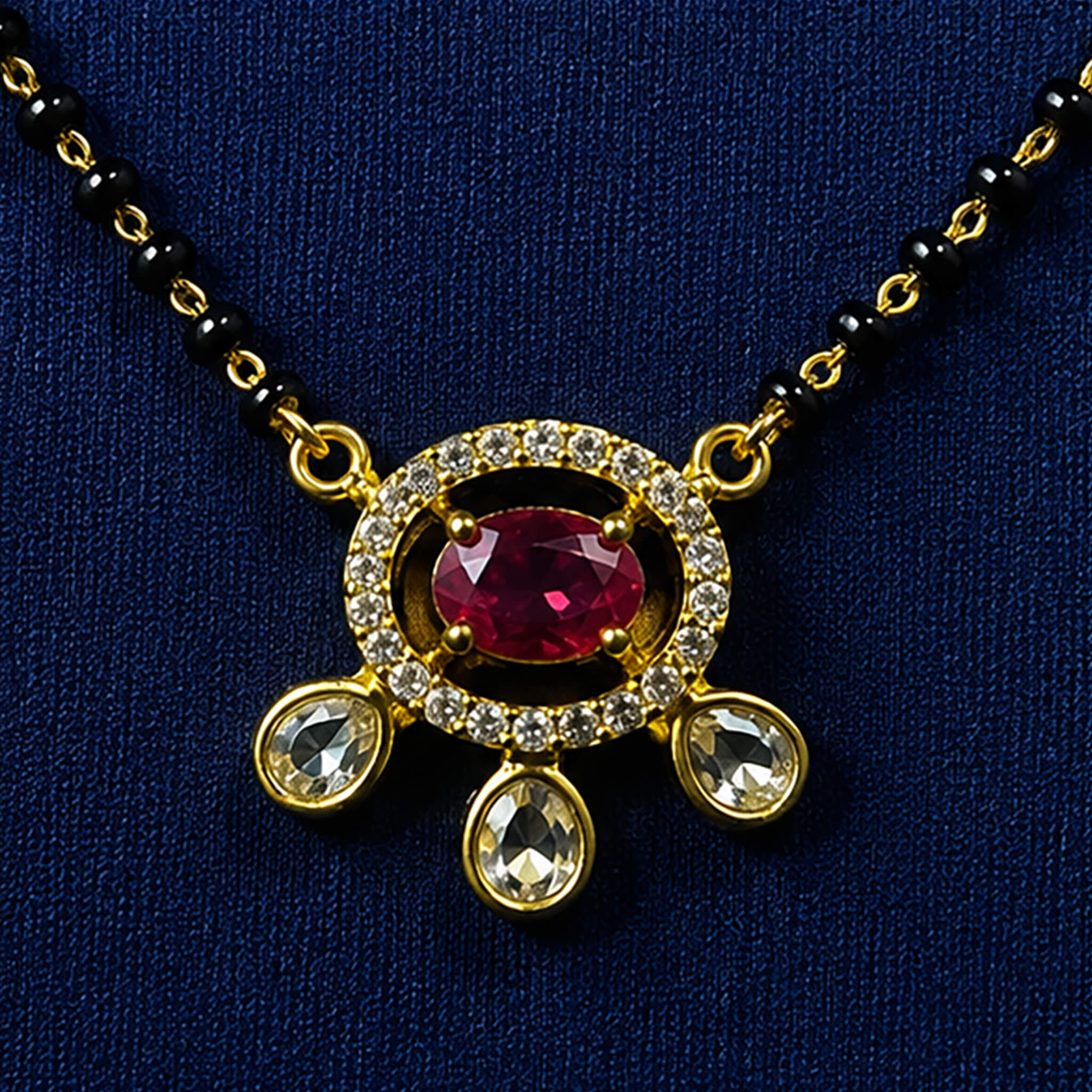Black-bead mangalsutra necklace with ruby-red stone pendant and dangling charms displayed on a royal blue velvet jewelry bust.