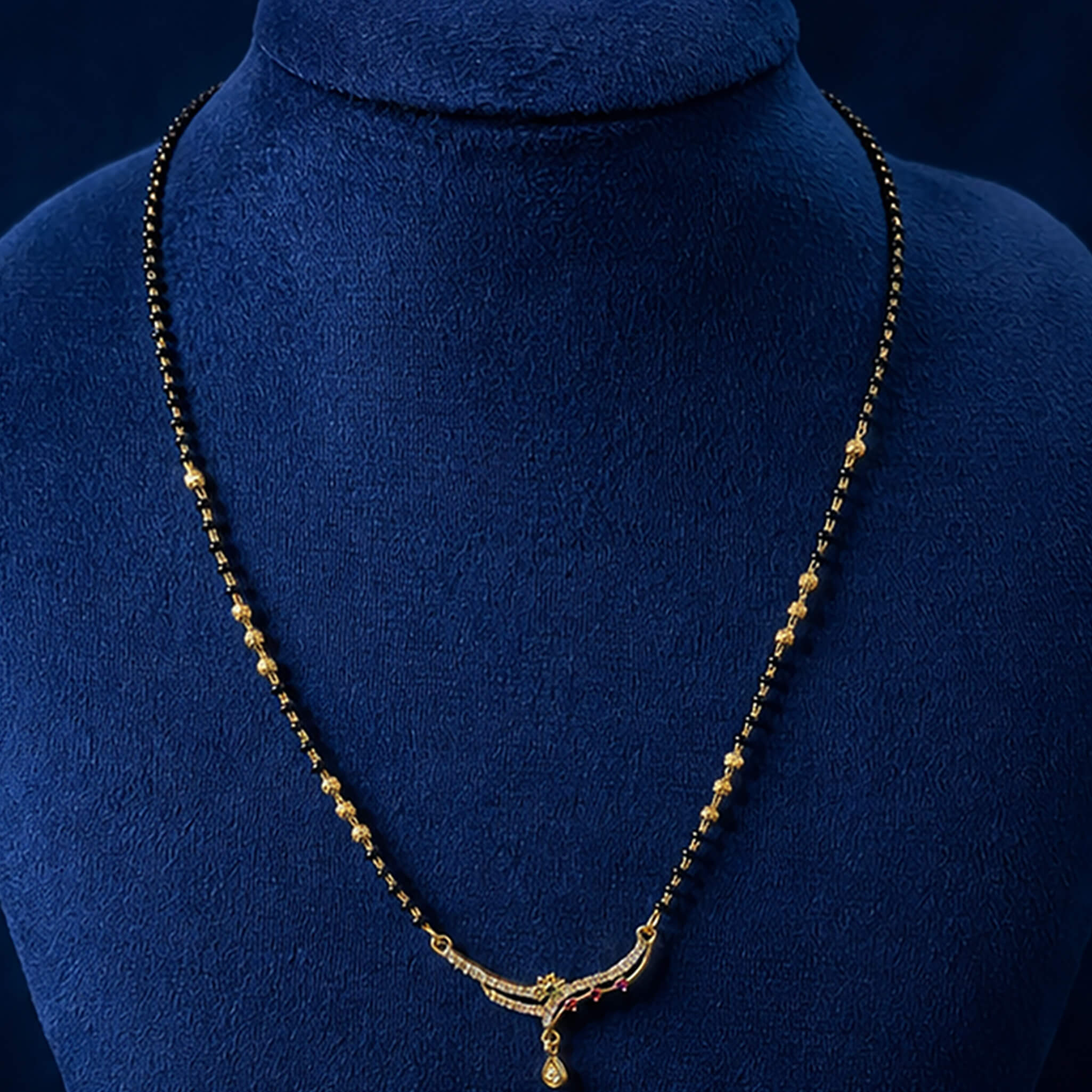 Black-bead mangalsutra necklace with ruby-red stone pendant and dangling charms displayed on a royal blue velvet jewelry bust.