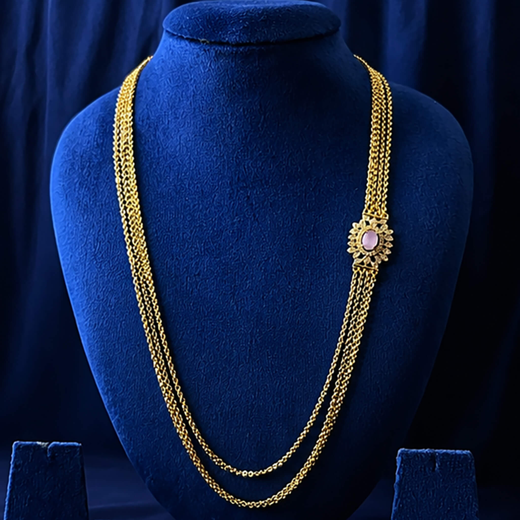 Traditional gold-tone Chandraharam with layered chains and pink floral accent displayed on a royal blue velvet jewelry bust.