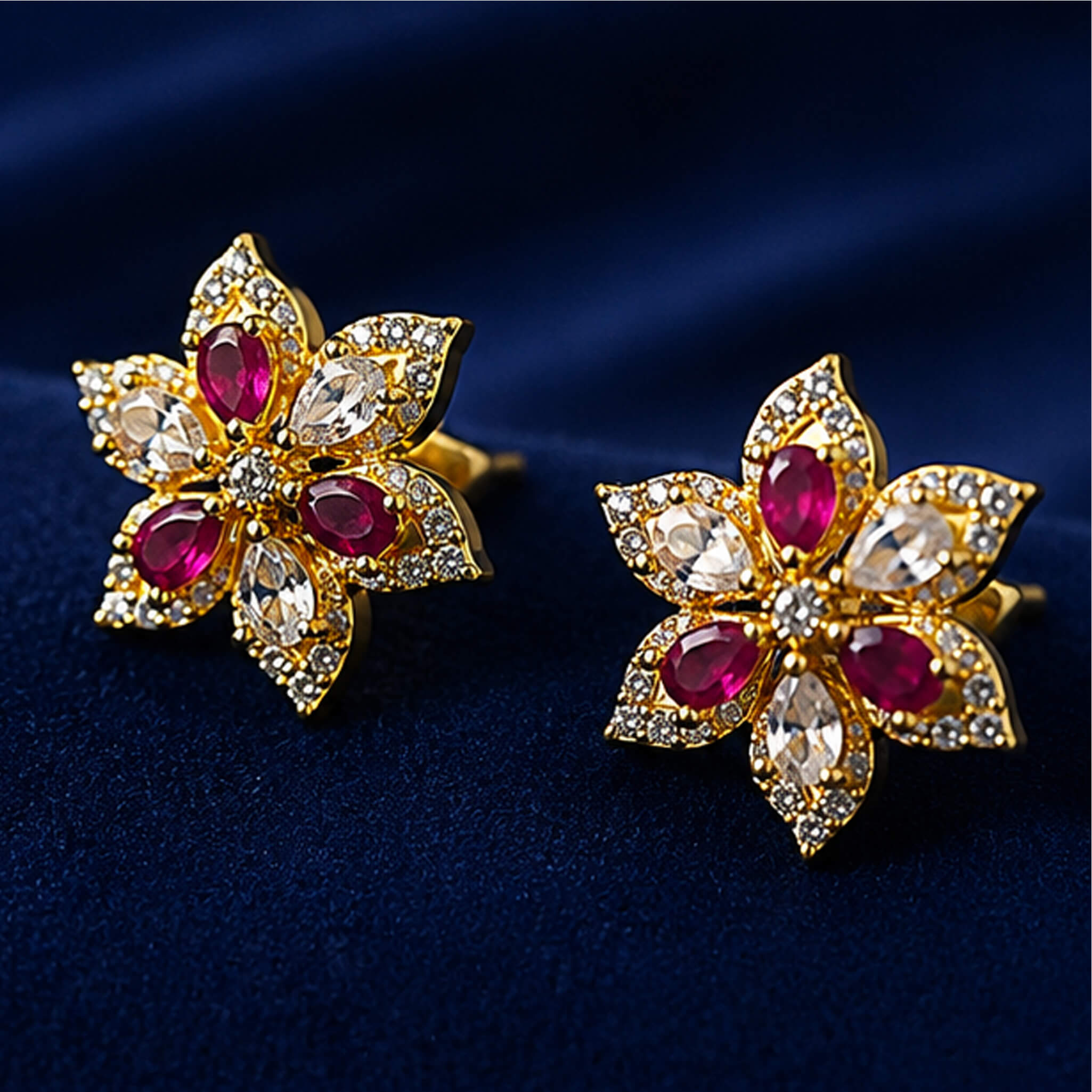Gold-tone floral stud earrings with ruby-red stones and crystal accents displayed on a royal blue velvet stand.