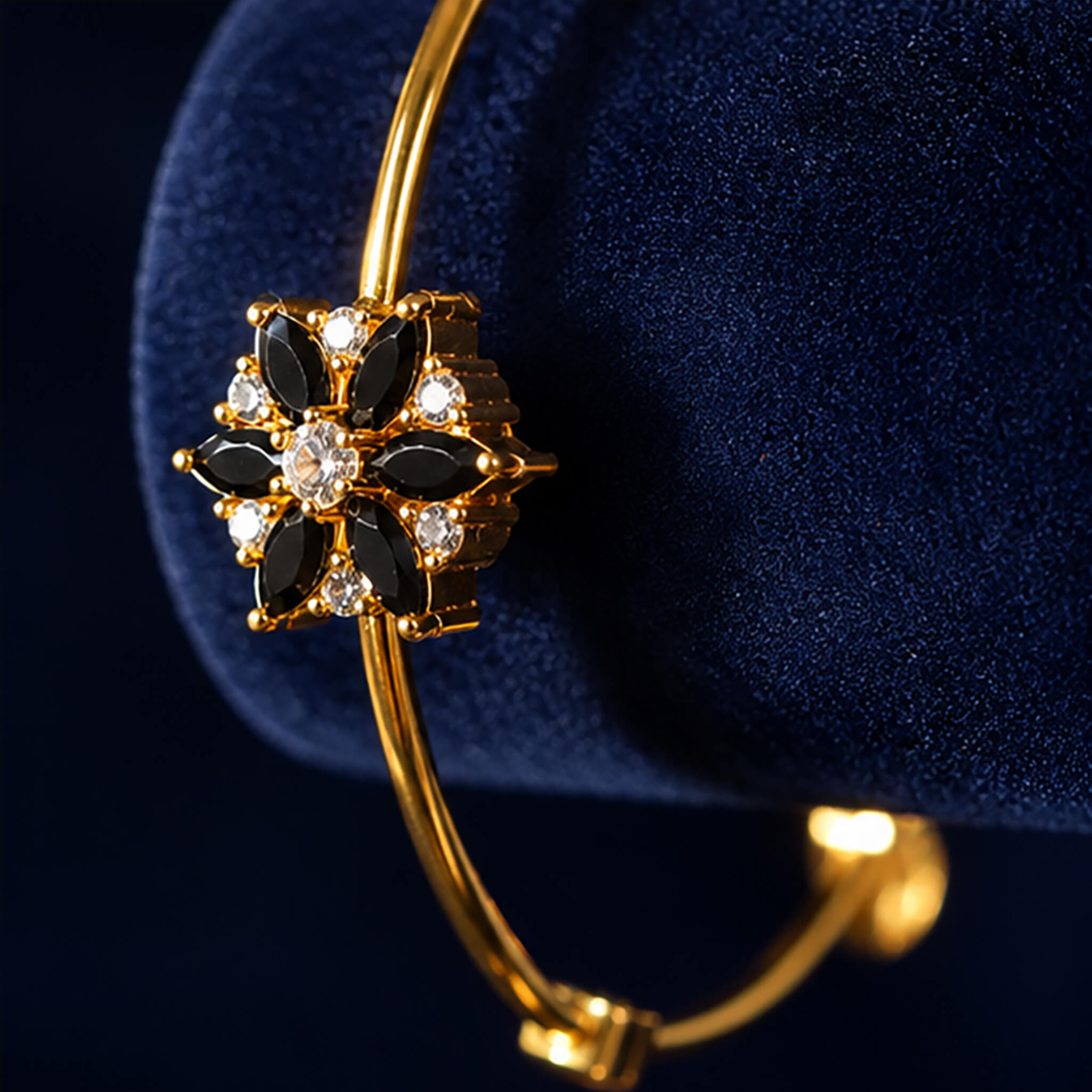 Gold-tone bracelet featuring a black floral stone centerpiece with sparkling crystal accents on a navy blue velvet background.