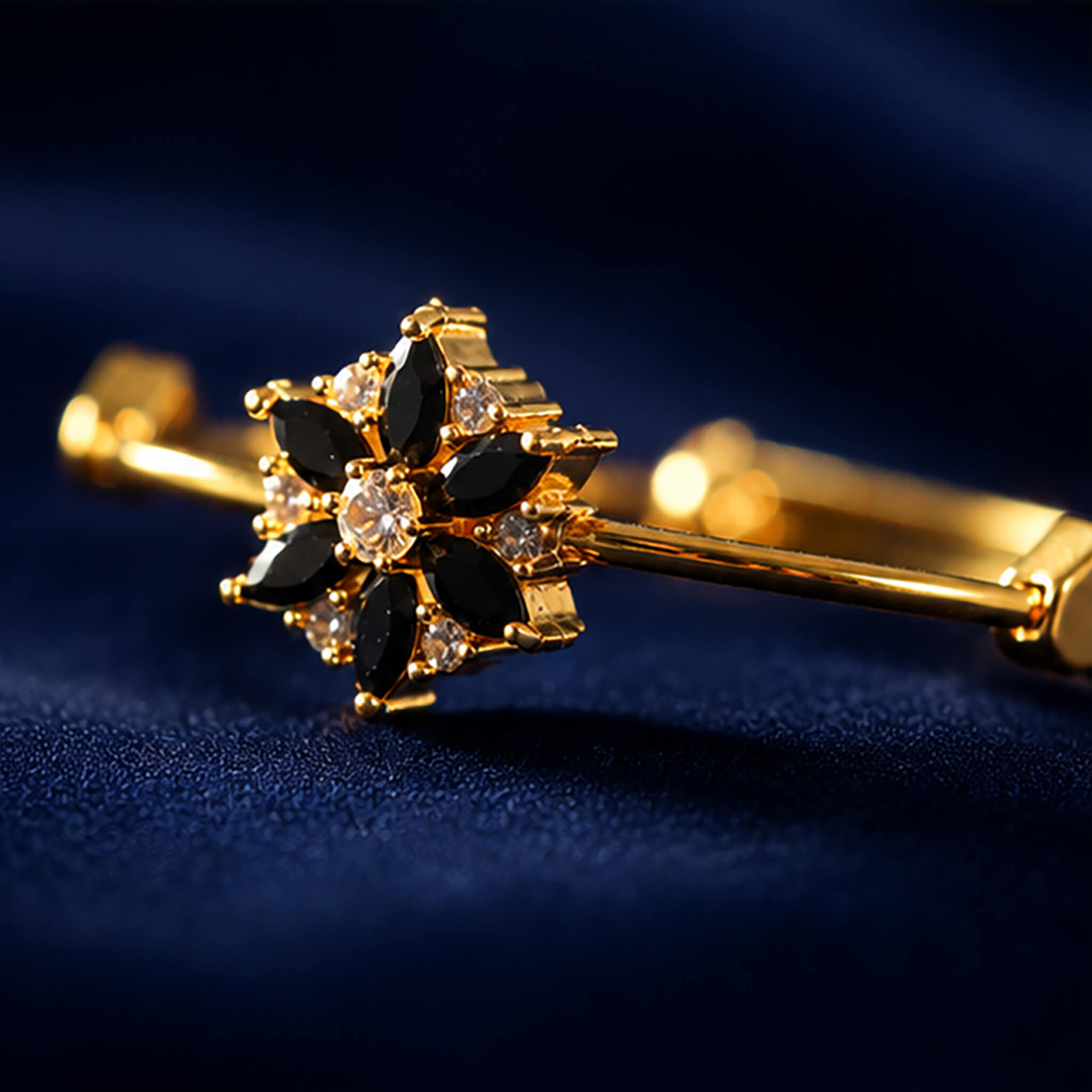 Gold-tone bracelet featuring a black floral stone centerpiece with sparkling crystal accents on a navy blue velvet background.