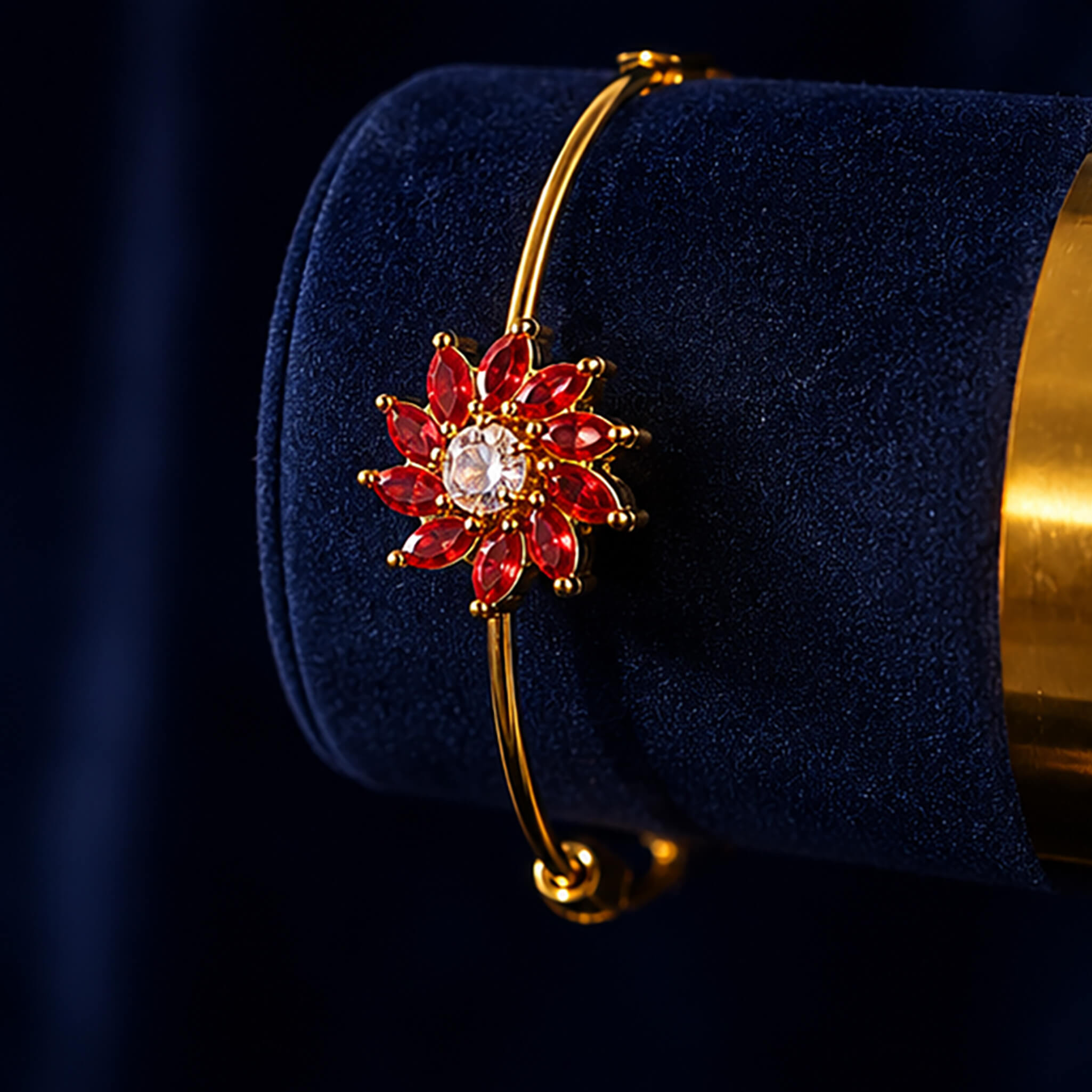 Gold-tone adjustable bracelet with ruby-red floral centerpiece and crystal stone on a luxurious dark blue background.
