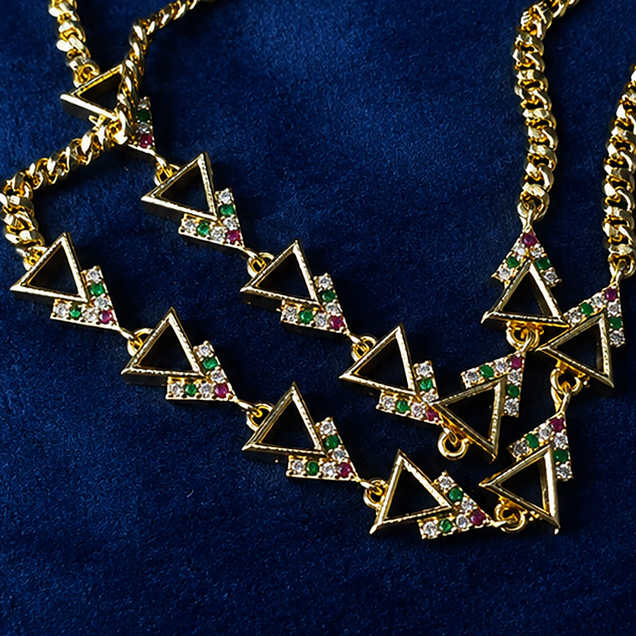 Double-layer gold-tone anklet with geometric triangle charms and colorful crystal accents displayed on a royal blue velvet background.