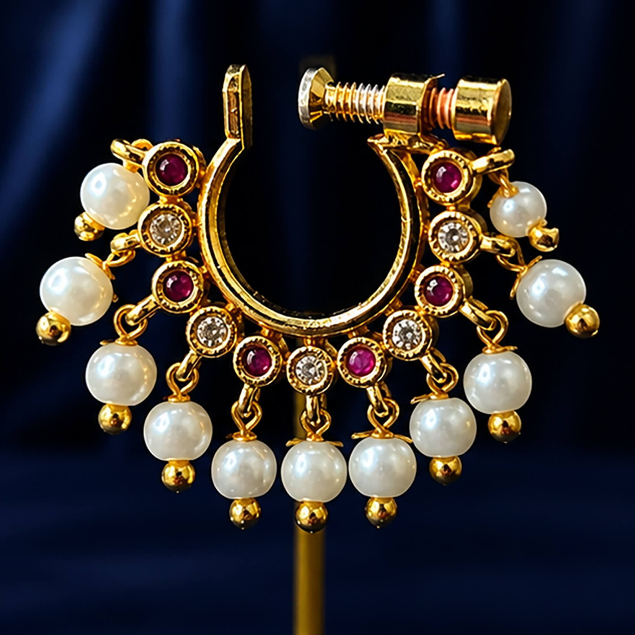 Traditional gold-tone nose ring with pearl drops, crystal accents, and ruby-colored stones displayed on a jewelry stand.