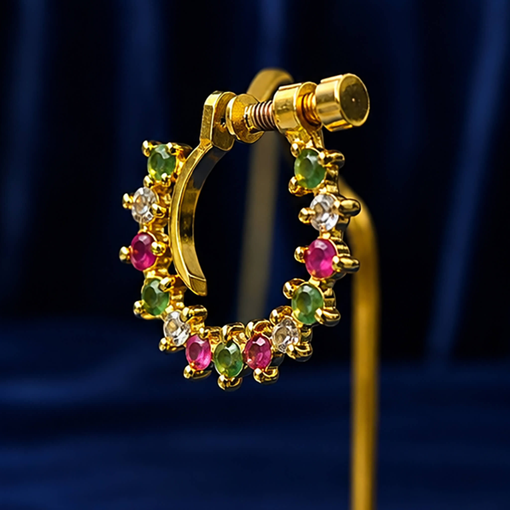Gold-tone crescent nose ring with emerald-green, ruby-pink, and crystal stones displayed on a royal blue velvet background. Image Title