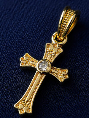 Gold-tone Christian cross pendant with decorative detailing and sparkling center stone on a royal blue velvet display.