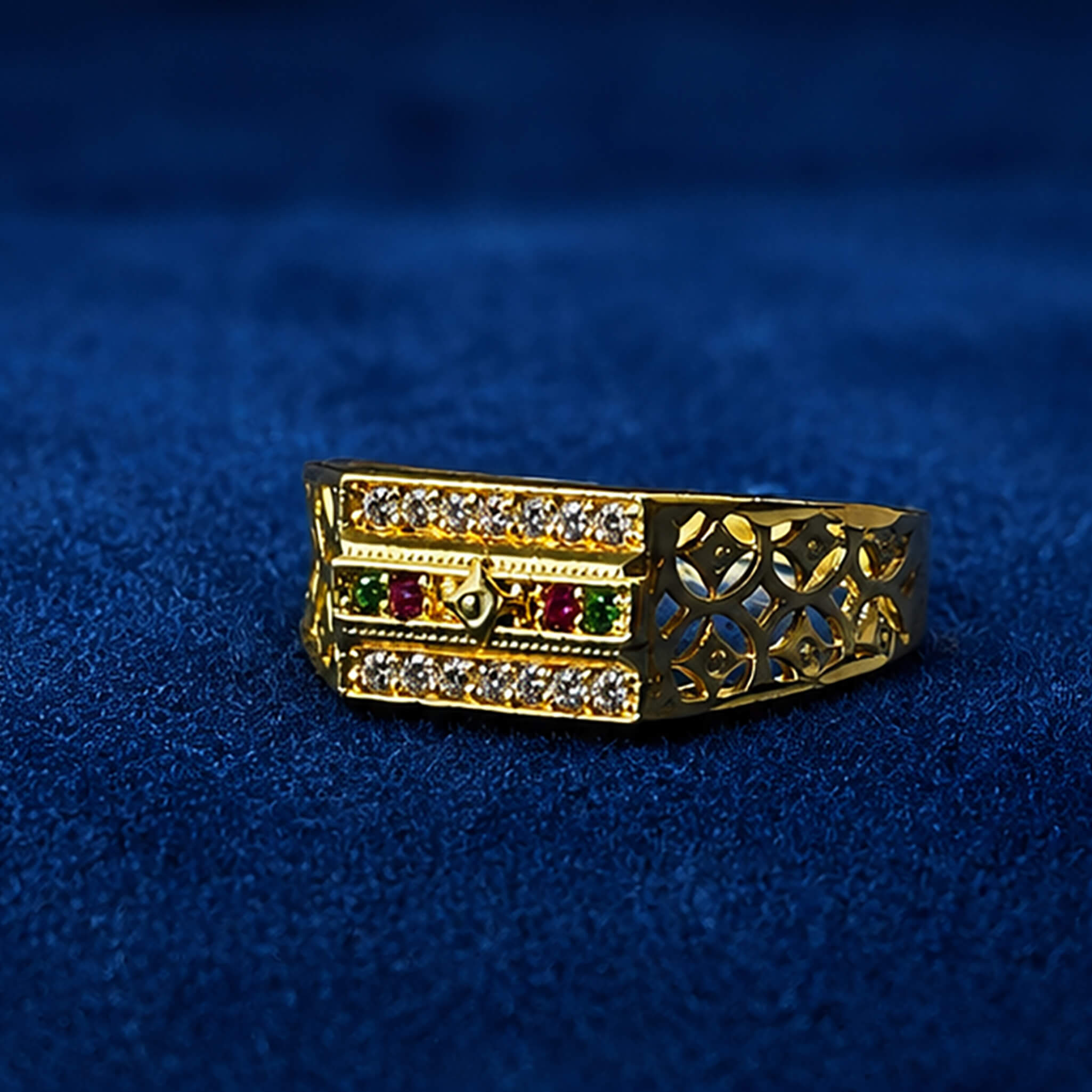 Gold-tone designer ring with sparkling crystal rows and ruby-green stone accents displayed on a royal blue velvet background.