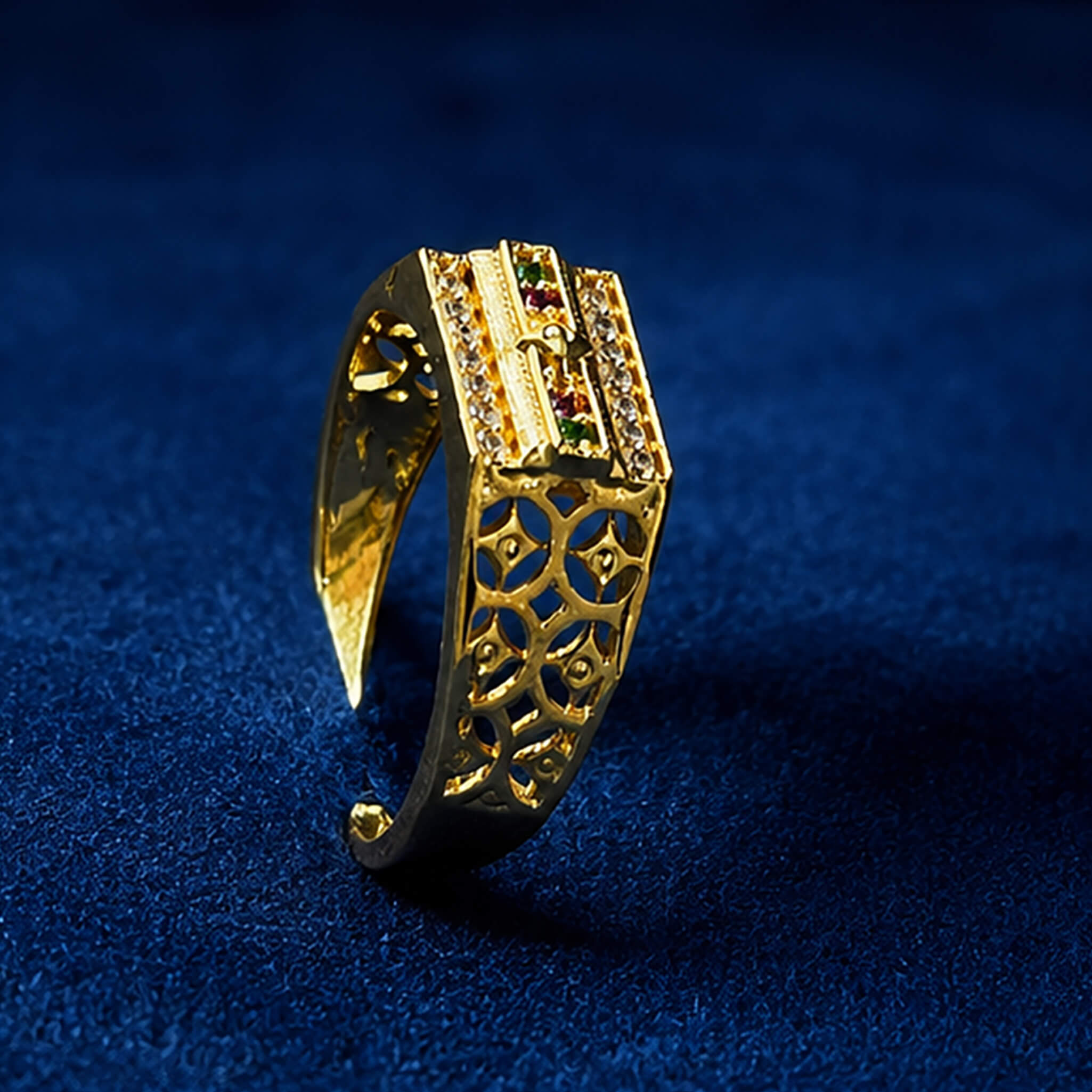 Gold-tone designer ring with sparkling crystal rows and ruby-green stone accents displayed on a royal blue velvet background.