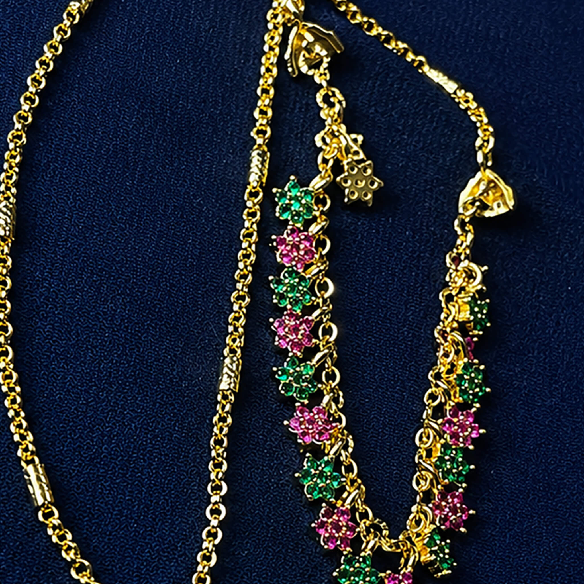 Gold-tone short chain featuring pink and green floral stone accents displayed on a royal blue velvet jewelry stand.