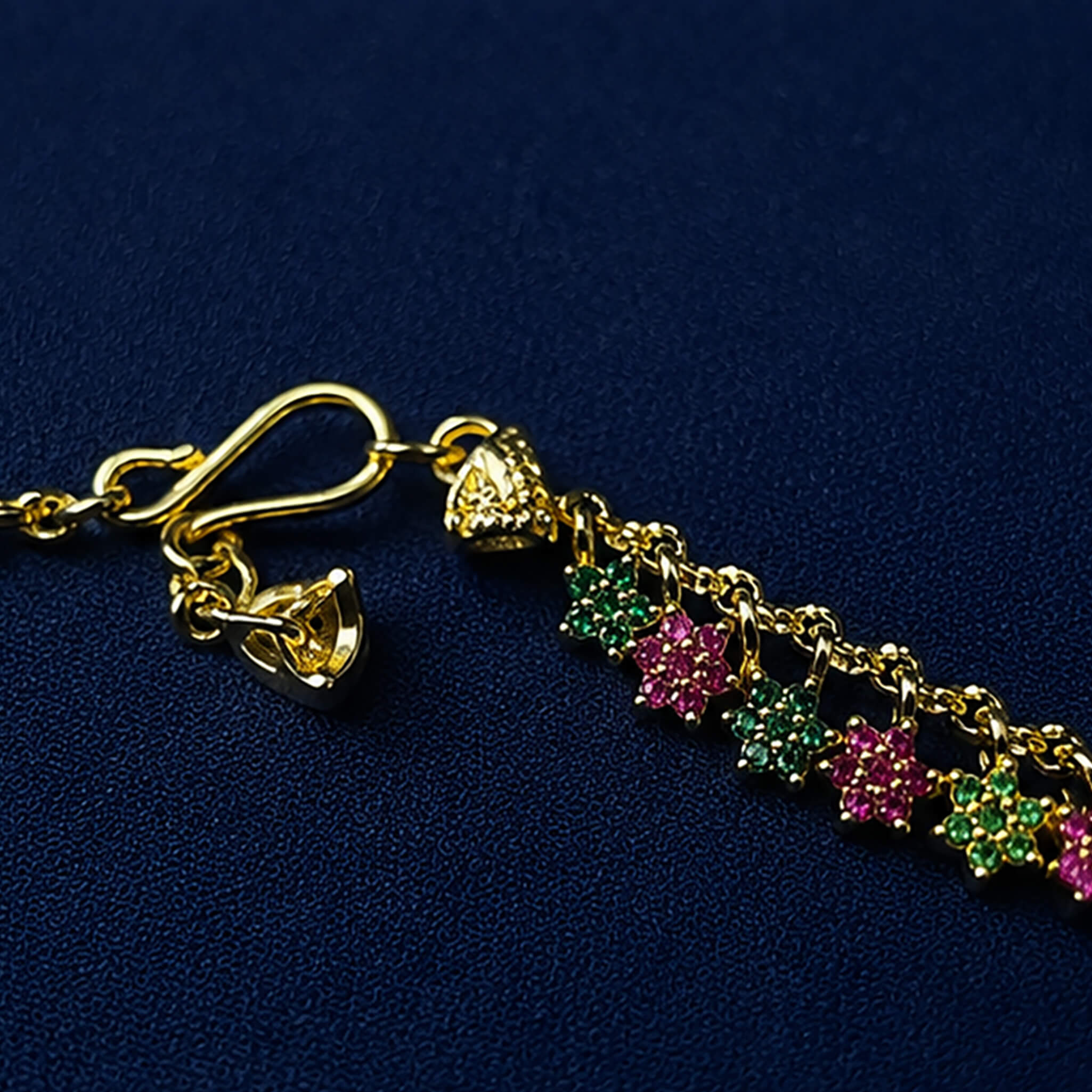 Gold-tone short chain featuring pink and green floral stone accents displayed on a royal blue velvet jewelry stand.