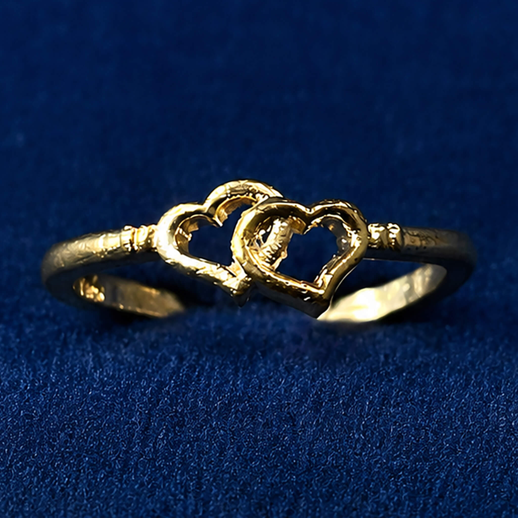 Gold-tone ring featuring intertwined heart designs displayed on a royal blue velvet background.