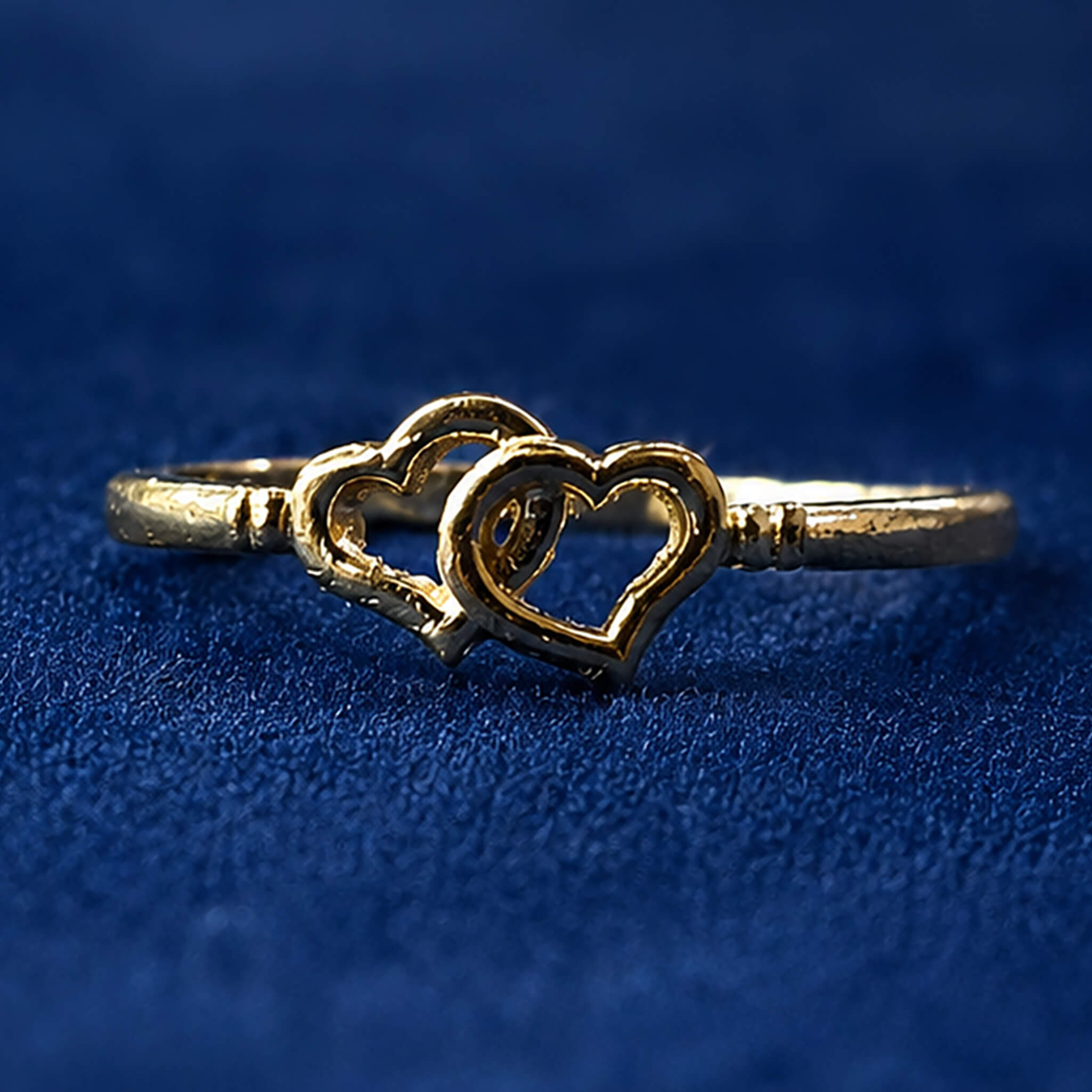 Gold-tone ring featuring intertwined heart designs displayed on a royal blue velvet background.