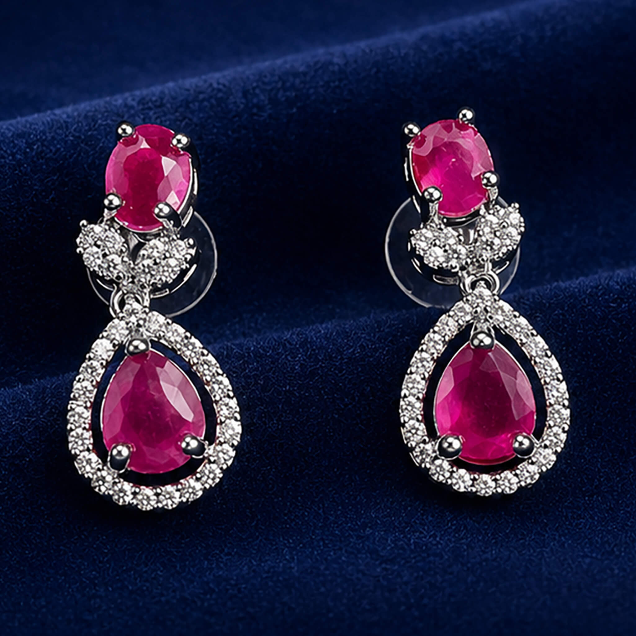 Elegant ruby-red stone necklace set with matching teardrop earrings displayed on a royal blue velvet jewelry stand.