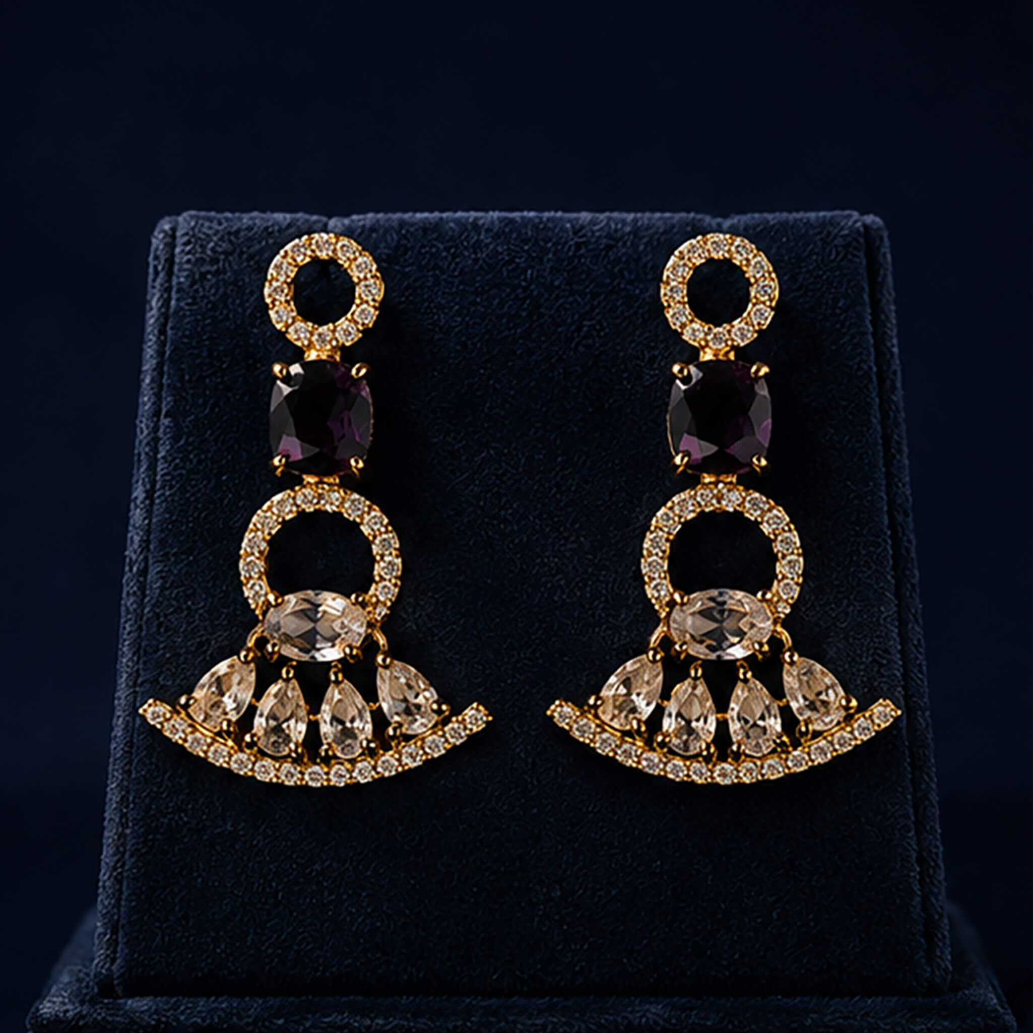 Gold-tone necklace and matching earrings set with amethyst-purple stones displayed on a luxury dark blue jewelry stand.