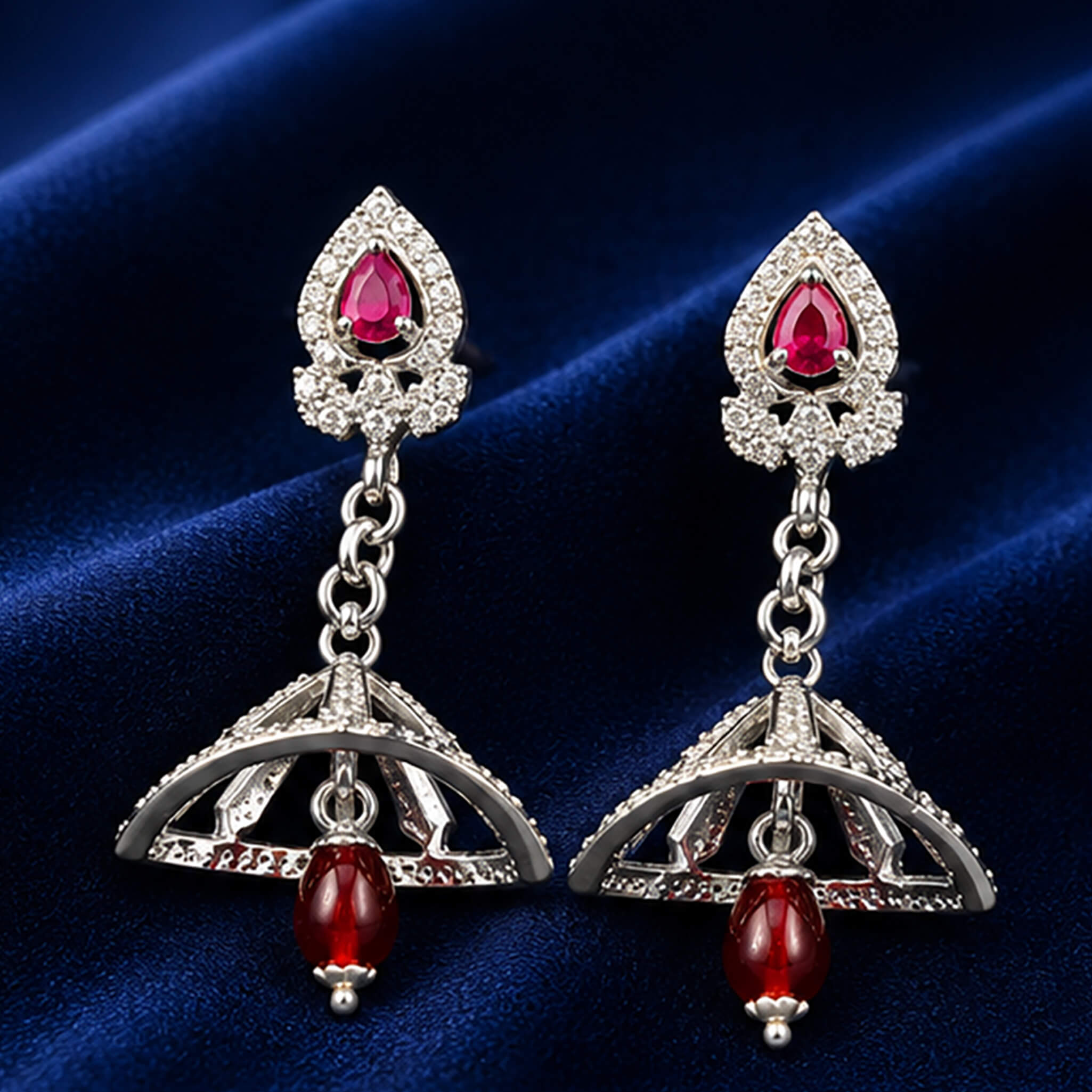 Silver-tone drop earrings featuring ruby-red stones and decorative dome-shaped drops displayed on a royal blue velvet stand.