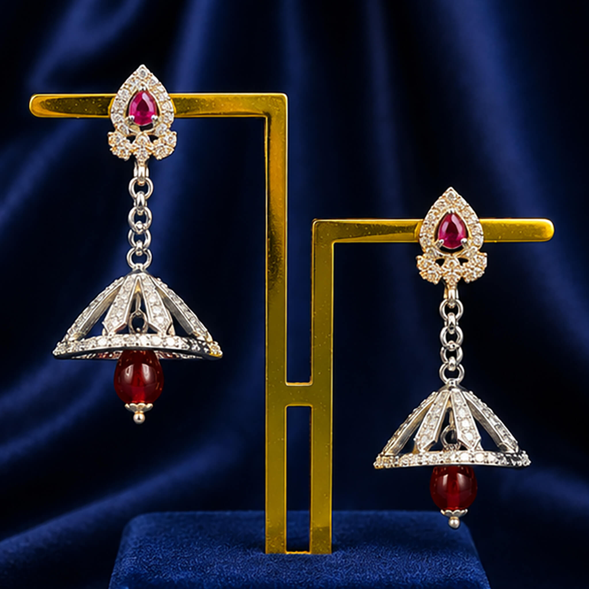 Silver-tone drop earrings featuring ruby-red stones and decorative dome-shaped drops displayed on a royal blue velvet stand.