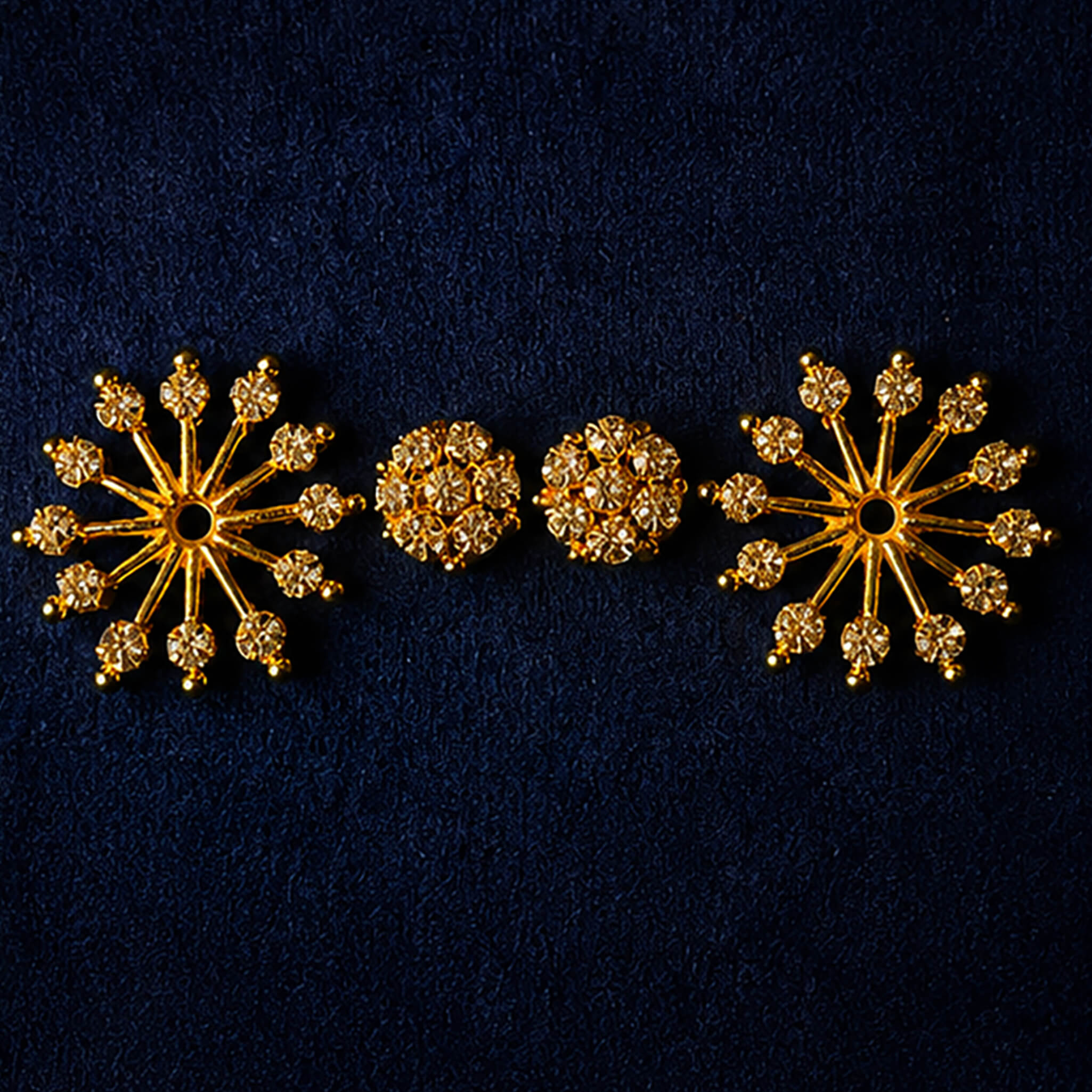 Gold-tone snowflake crystal stud earrings with sparkling stones displayed on a luxury dark blue background.