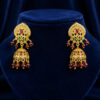 Gold-tone traditional jhumka earrings with ruby-red stones, crystal embellishments, and garnet bead danglers displayed on a royal blue velvet stand.