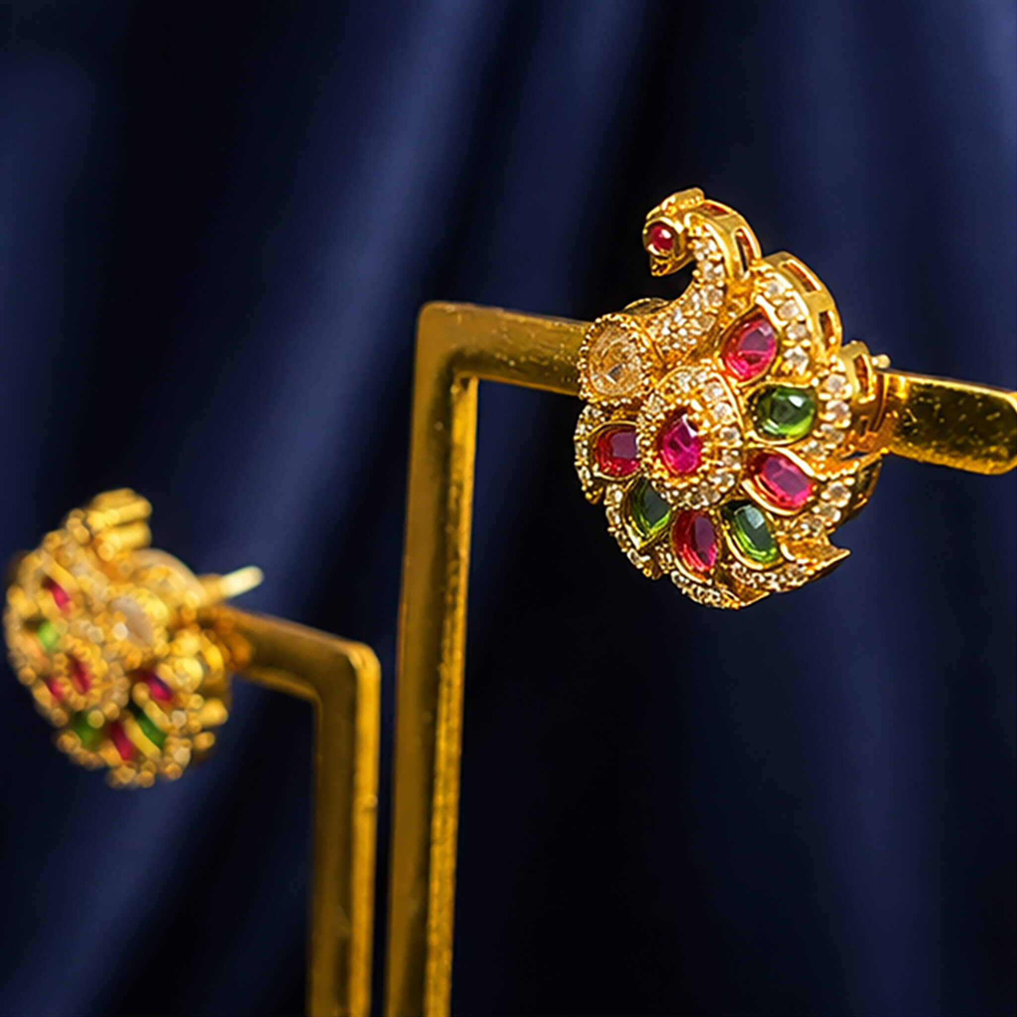 Gold-tone floral ear tops featuring pink ruby stones, green emerald stones, and sparkling crystal accents on a royal blue background.